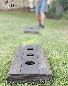 a man standing next to a wooden board on top of a grass covered field with holes in it