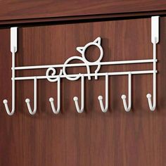 a wall mounted coat rack with five hooks and a cat on the top hook, hanging from it's side