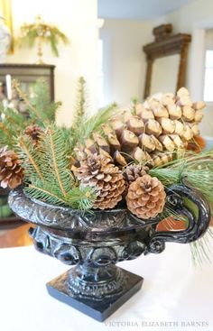 pine cones and evergreen branches in an ornate urn on a dining room table with mirror