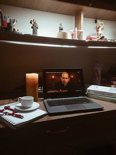 an open laptop computer sitting on top of a desk next to a cup and saucer