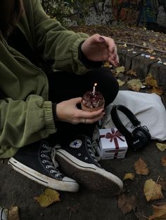 a person sitting on the ground holding a small cake with a candle in their hand