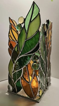 a stained glass vase sitting on top of a white table next to a green plant