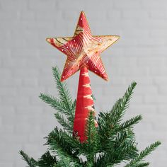 an ornament shaped like a star on top of a christmas tree in front of a brick wall