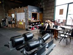 people are sitting at tables in an industrial setting with large black objects on the floor