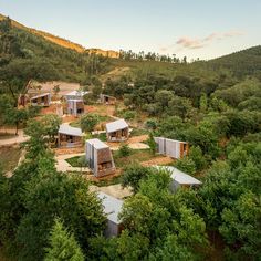 an aerial view of several small houses in the middle of trees and bushes, with mountains in the background