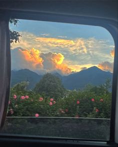 the sun is setting over mountains as seen from inside a train window with pink flowers in the foreground