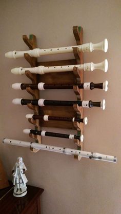 a wall mounted instrument rack with several flutes on it's side and a small white figurine next to it