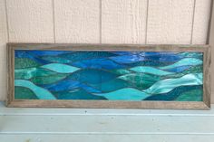 a blue and green stained glass window sitting on top of a wooden frame next to a wall