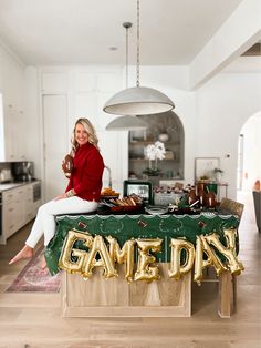 a woman sitting on top of a table holding a wine glass in front of a game day sign