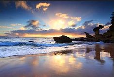 the sun is setting over some rocks on the beach