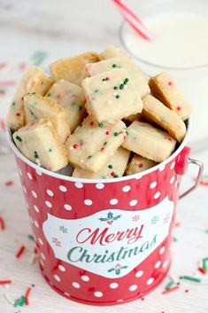 a red bucket filled with christmas shortbreads next to a glass of milk