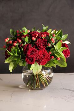 a vase filled with red roses and greenery on top of a marble countertop