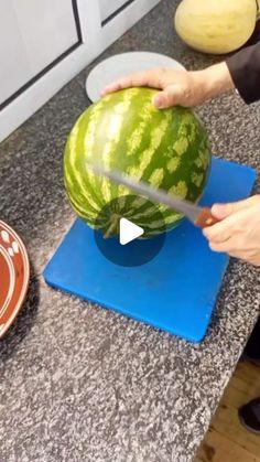 a person cutting up a watermelon on top of a blue mat in a kitchen