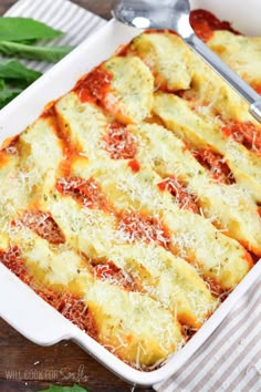 a casserole dish with cheese and sauce in it on a striped cloth next to a spoon