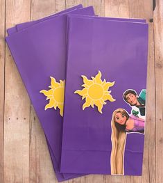 two purple paper bags with pictures of people and the sun on them sitting on a wooden surface