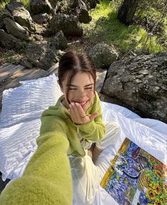 a young woman sitting on top of a white blanket next to a forest filled with trees