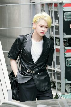 a young man with blonde hair wearing a black leather jacket and carrying a handbag