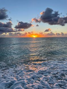 the sun is setting over the ocean with clouds in the sky and waves on the beach