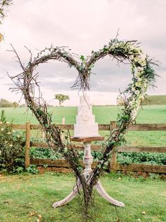 a heart shaped cake sitting on top of a wooden stand in the middle of a field