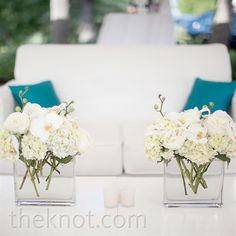 two vases filled with white flowers sitting on top of a table next to a couch