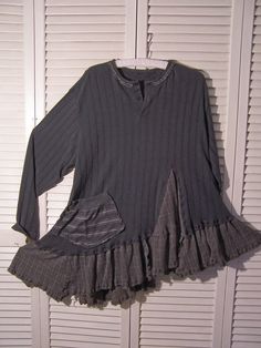 a gray shirt with ruffles on the bottom and long sleeves is hanging up against a white wall