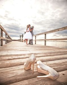 a bride and groom standing on a pier with their wedding shoes in the foreground