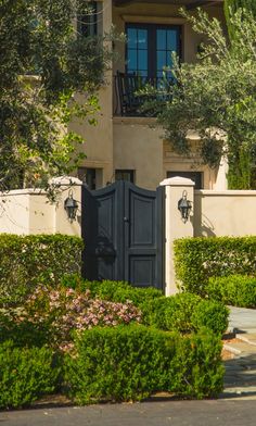 an entrance to a house with bushes and trees around it, in front of a gate