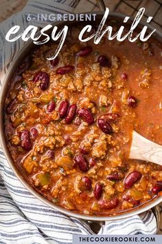 a pot filled with chili and beans on top of a striped towel next to a wooden spoon