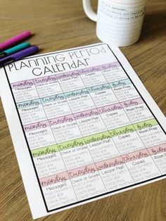 a calendar sitting on top of a wooden table next to a cup and two markers