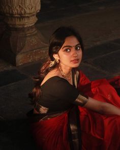 a woman sitting on the ground in a red skirt and black top with gold jewelry