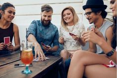 group of people sitting around a table looking at their cell phones and drinking beverages in front of them