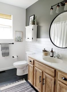 a white toilet sitting next to a bathroom sink under a round mirror in a bathroom