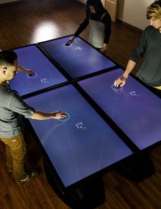 three people standing in front of a table with four different colors on it and one person pointing at the screen