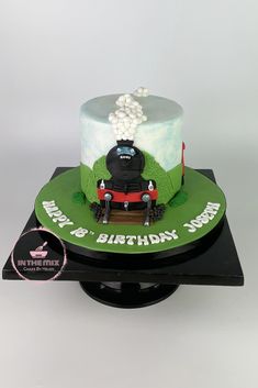 a birthday cake with a train on the top and green frosting, sitting on a black stand