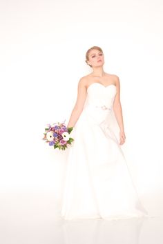 a woman in a white wedding dress holding a bouquet of flowers and posing for the camera