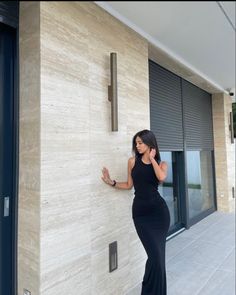 a woman in a black dress leaning against a wall