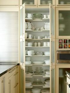 an open refrigerator in a kitchen with dishes and cups on the shelves next to it