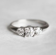 three stone diamond ring sitting on top of a white surface with no one around it