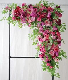 an arrangement of pink and red flowers on a black stand with greenery around it