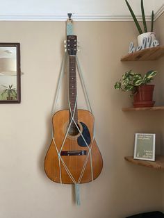 an acoustic guitar hanging on the wall next to a potted plant in a corner