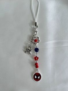 a spiderman keychain is hanging on a white sheet with red, blue and black beads