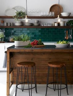 two stools sit at the center of a kitchen island in front of an open shelving