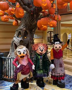 three characters dressed in costumes standing under a tree with pumpkins hanging from it's branches