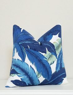 a blue and white pillow with palm leaves on the front, sitting on a table