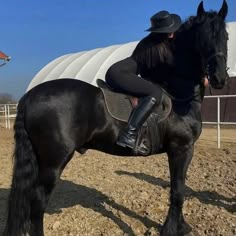 a woman riding on the back of a black horse in an enclosed area next to a white building