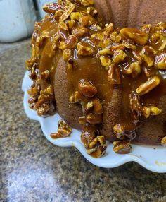 a bundt cake covered in caramel and pecans on a white platter