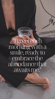 a woman sitting on the floor holding a glass with her hand in her lap and saying, i great each morning with a smile ready to embrace the abundance that awaits me