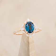 a ring with a blue stone surrounded by white diamonds on top of a wooden stand