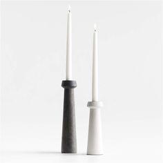 two white candles sitting next to each other in front of a white background with one black candle