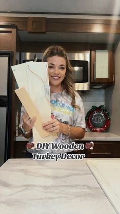 a woman standing in front of a kitchen counter holding up a piece of cardboard with the words diy wooden turkey decor on it